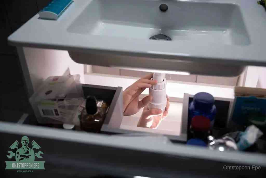 Een pompfles met zeep boven een wastafel, de heet water en afwasmiddel-methode om een vetprop in de afvoer los te maken in Epe