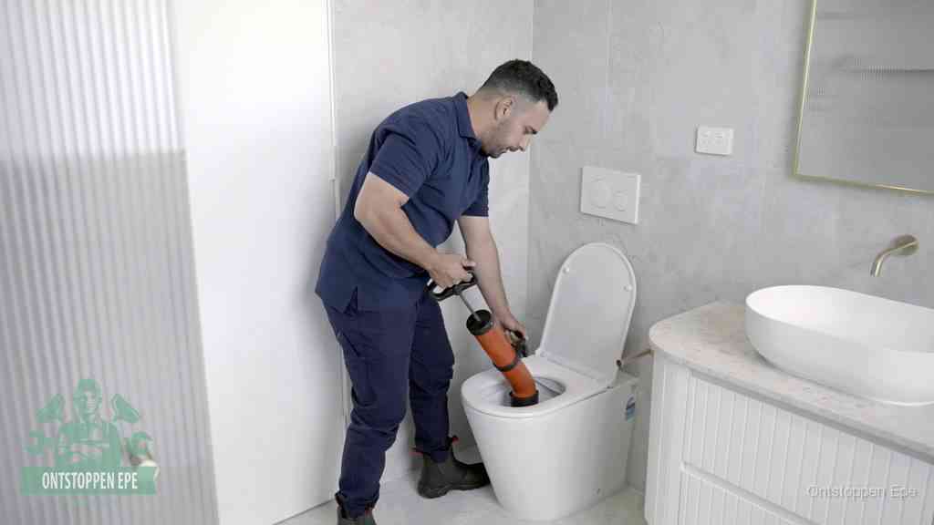 Een monteur buigt over een wandcloset en duwt met de hand een persluchtontstopper in de toiletpot om de verstopping handmatig los te maken in Epe