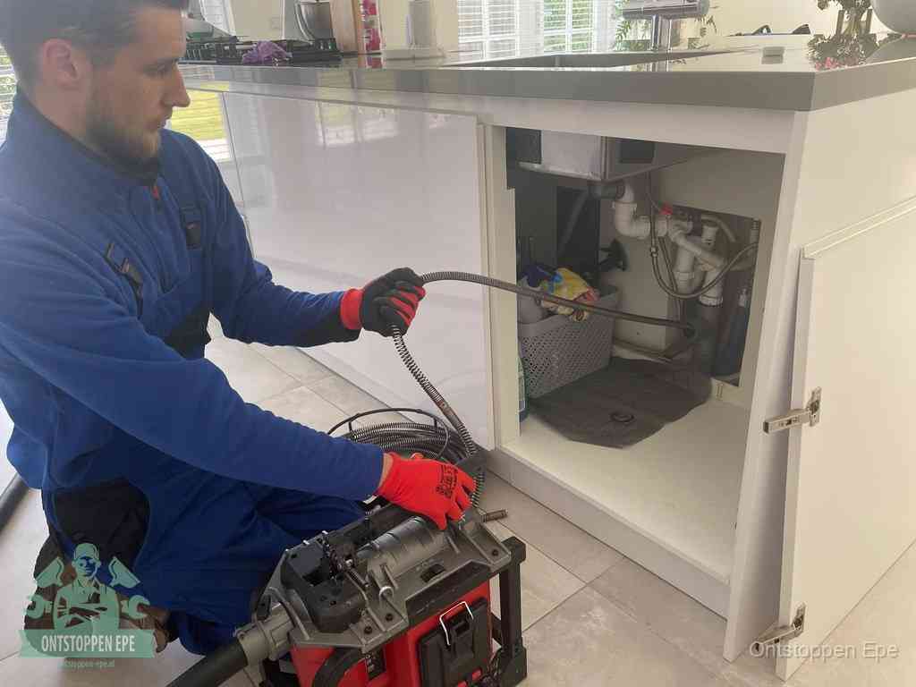 Monteur voert een ontstoppingsveer in de afvoer onder de keuken in Epe