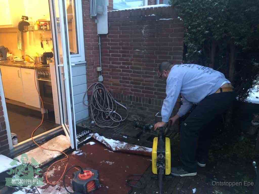 Een monteur werkt buiten bij een open riool-/grondput met een elektrische ontstoppingsmachine om een verborgen afvoerprobleem op te sporen in Epe