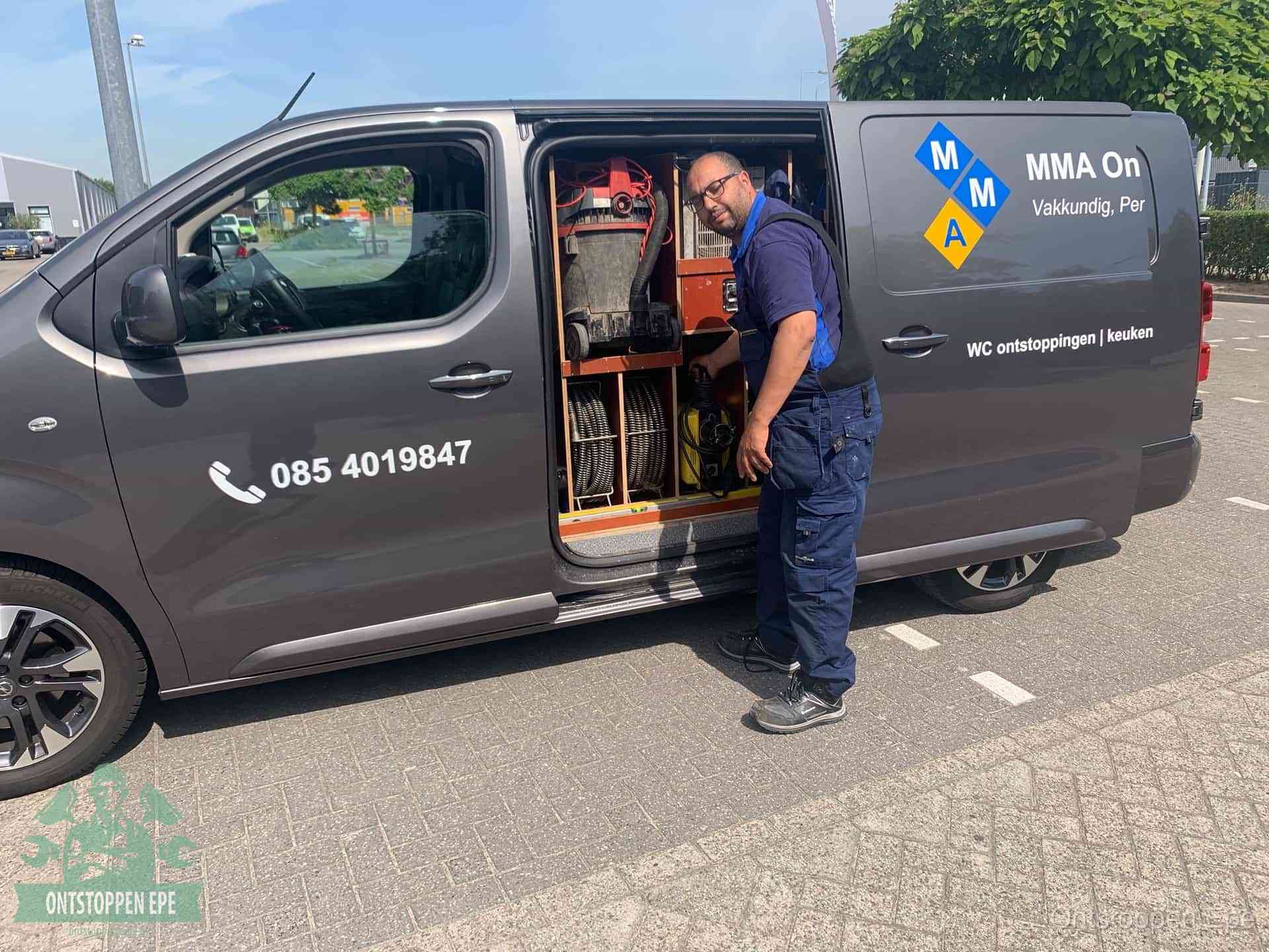 Een monteur bij de open schuifdeur van zijn bedrijfsbus op een parkeerplaats, klaar om de oorzaak van terugkerende afvoerverstoppingen aan te pakken in Epe