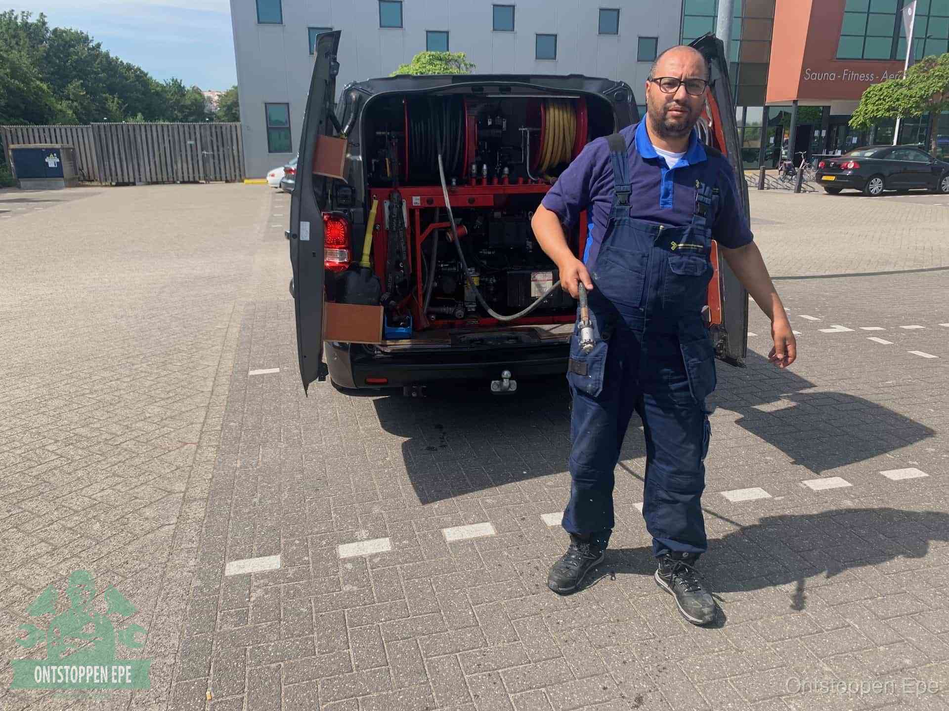 Een monteur bij zijn bestelbus met een hogedruk- en rioolreinigingsunit, klaar om de oorzaak van terugkerende wc-verstoppingen aan te pakken in Epe
