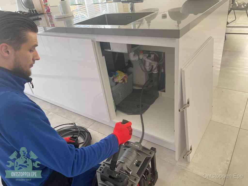 Monteur ontstopt met een veermachine een verstopte afvoer onder de gootsteen in Epe