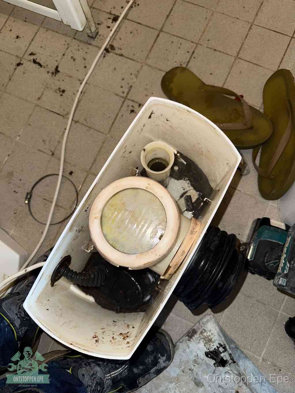 Een gedemonteerde toiletpot op de vloer met ontstoppingsveer en gereedschap ernaast, het verwijderen van een vastzittend voorwerp uit de wc in Epe