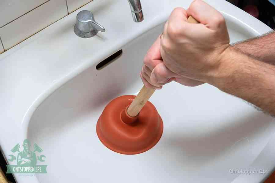 Twee handen gebruiken een rode rubberen plopper op een sanitair-afvoer om het toilet te ontstoppen in Epe