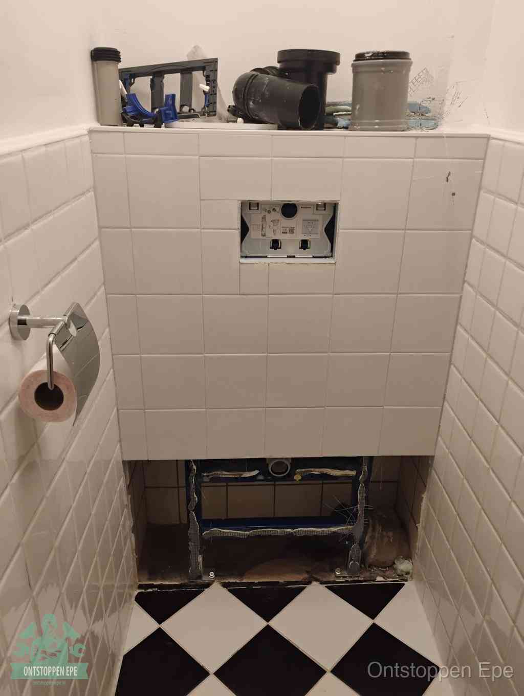 Een toiletruimte waar het hangtoilet en de inbouwreservoir-onderdelen zijn vrijgelegd voor onderhoud, periodiek nazicht voorkomt een wc-verstopping in Epe