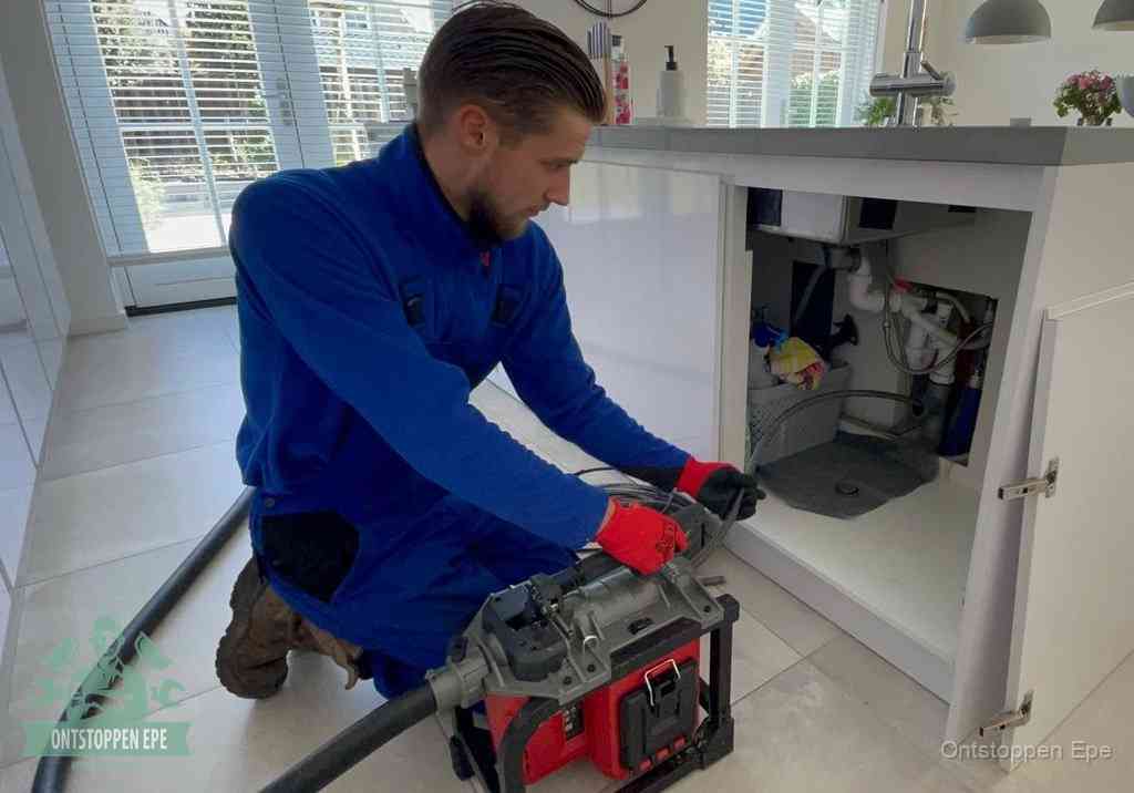 Een monteur voert een professionele elektrische ontstoppingsmachine in de afvoer onder de spoelbak tijdens het gootsteen ontstoppen in Epe